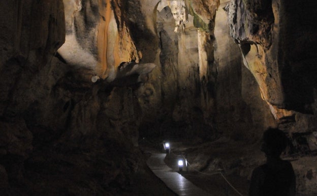 Imagen principal - Arriba, un visitante observa los altos techos de la sala de la Ermita. Abajo a la izquierda, la plataforma de madera, que se encuentra iluminada por pequeños faroles. Abajo a la derecha, formaciones en las paredes de la gruta. 