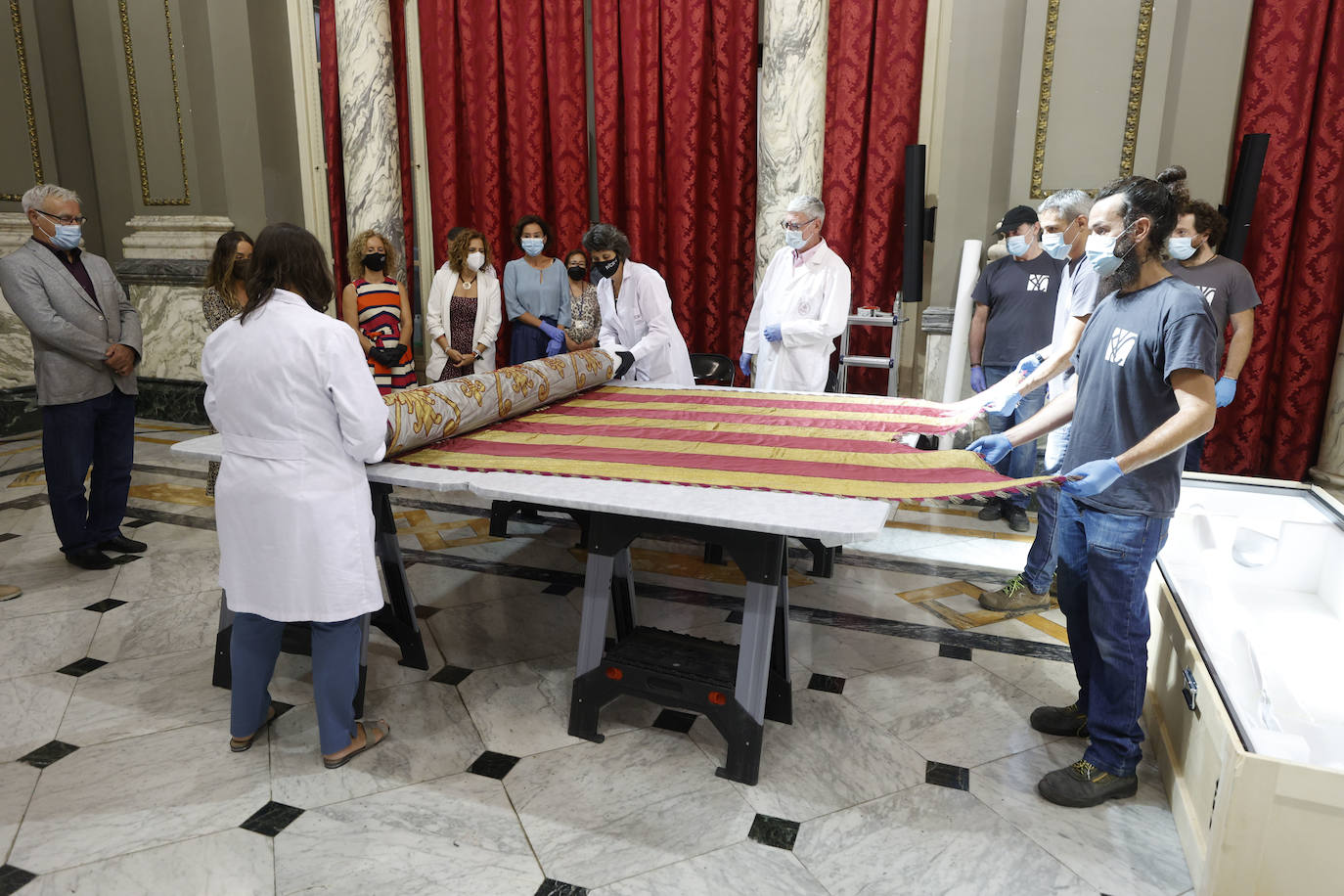 Cuatro meses de restauración devuelven el brillo a la enseña de 1928, que procesionará el 9 d'Octubre. Los expertos comprueban que el azul grisáceo que corona la pieza responde al mismo tono que muestra la bandera del siglo XVI