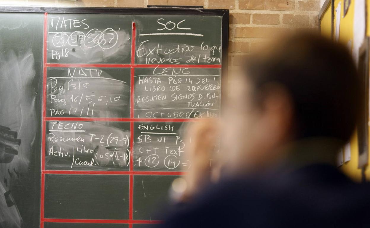 Un alumno en clase, con las tareas a realizar anotadas en la pizarra. 