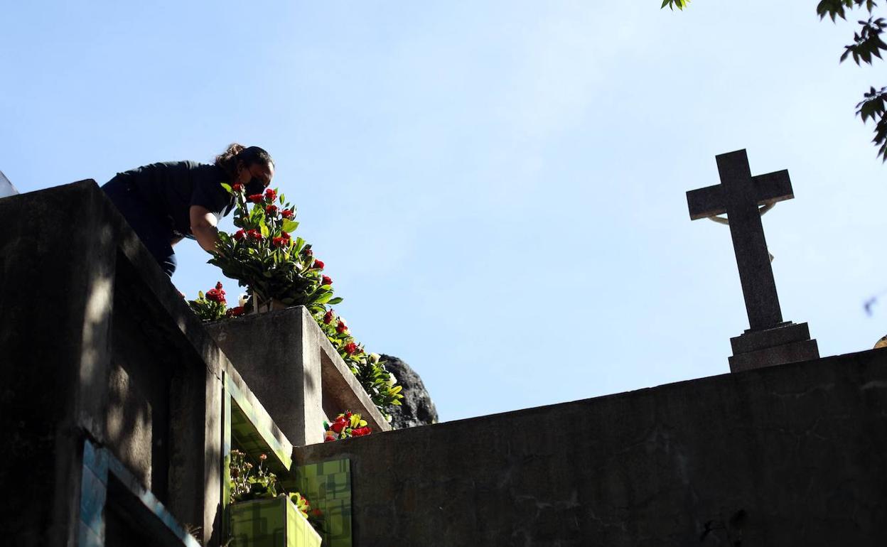 Una mujer coloca flores en una tumba. 