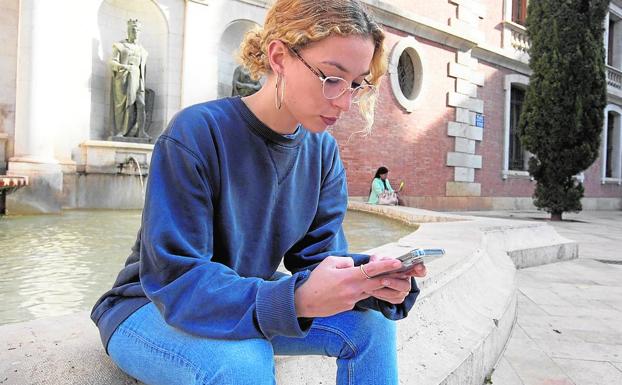 Entre redes. Violeta Anduig consulta la red social en su teléfono móvil, sentada en una fuente del centro de Valencia.