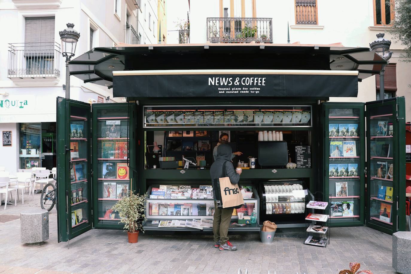En la plaza Doctor Collado de Valencia se encuentra el que, hasta la fecha, es el único de los nuevos quioscos que comienzan a verse en España. Se trata de establecimientos que ya se abren paso en Barcelona y Madrid y que combinan la venta de prensa con el café de especialidad. Los lectores pueden encontrar periódicos y revistas especializadas mientran disfrutas de un café para llevar, un modo de compra que cada vez gana más adeptos en la ciudad. 