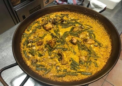 Imagen secundaria 1 - Arriba, Mel sostiene una botella en la bodega el restaurante. A la izquierda, la paella tradicional que se cocina en Ca Xoret y, a la derecha, una parte del monumental belén que han montado este año. 