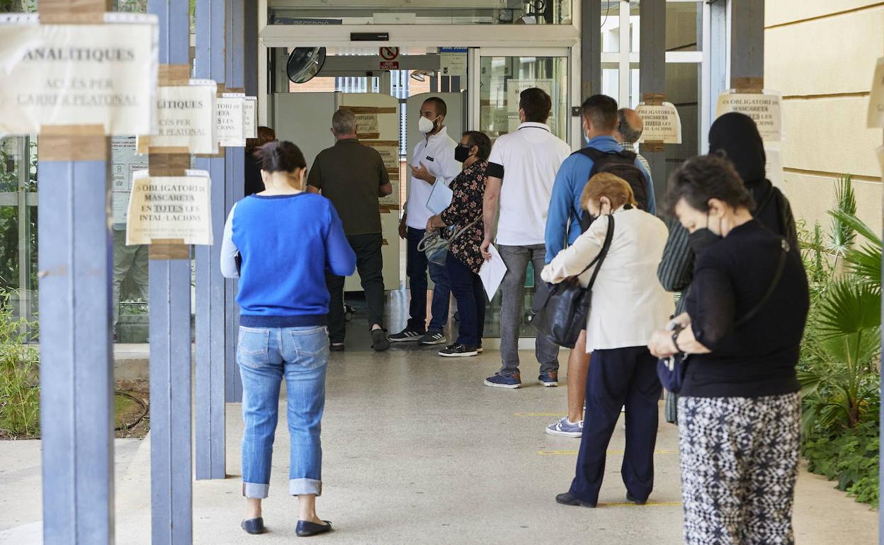 varias personas hacen cola e n un centro de salud. 