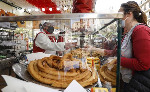 Una mujer compra en un puesto de churros y buñuelos en las Fallas 2022.