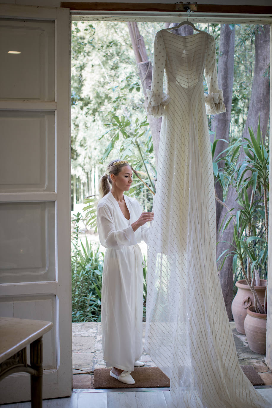 El vestido es de crep con escote cuadrado y falda recta. Las mangas y el sobre vestido que hace la cola son de organza de seda y algodón bordado con pequeñas paillettes dorado mate.