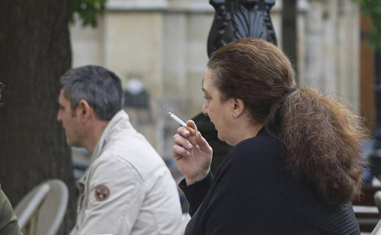 Una mujer fuma en una terraza. 