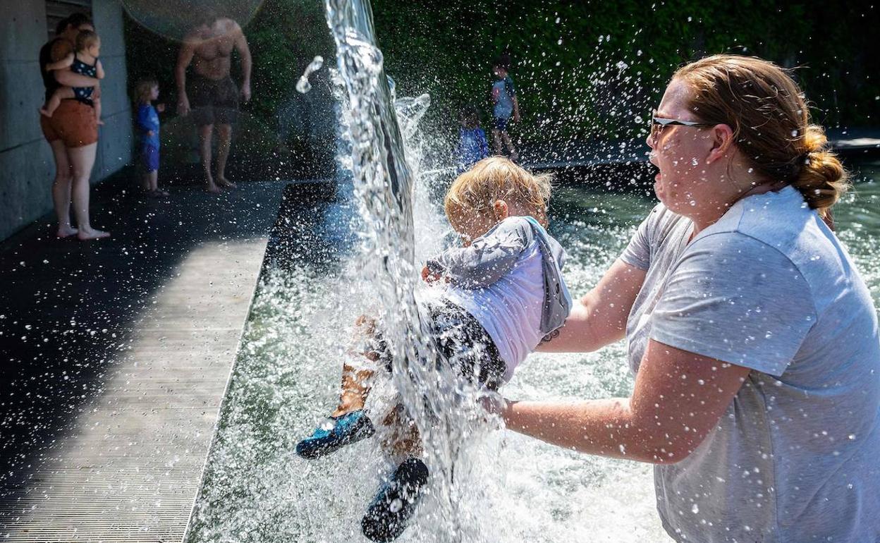 Una mujer refresca a su bebé en una fuente.