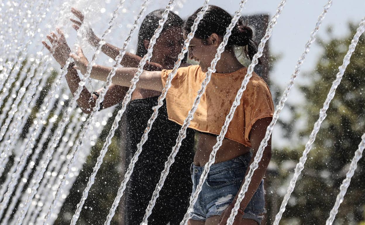 Dos jóvenes se refrescan en una fuente en Valencia. 