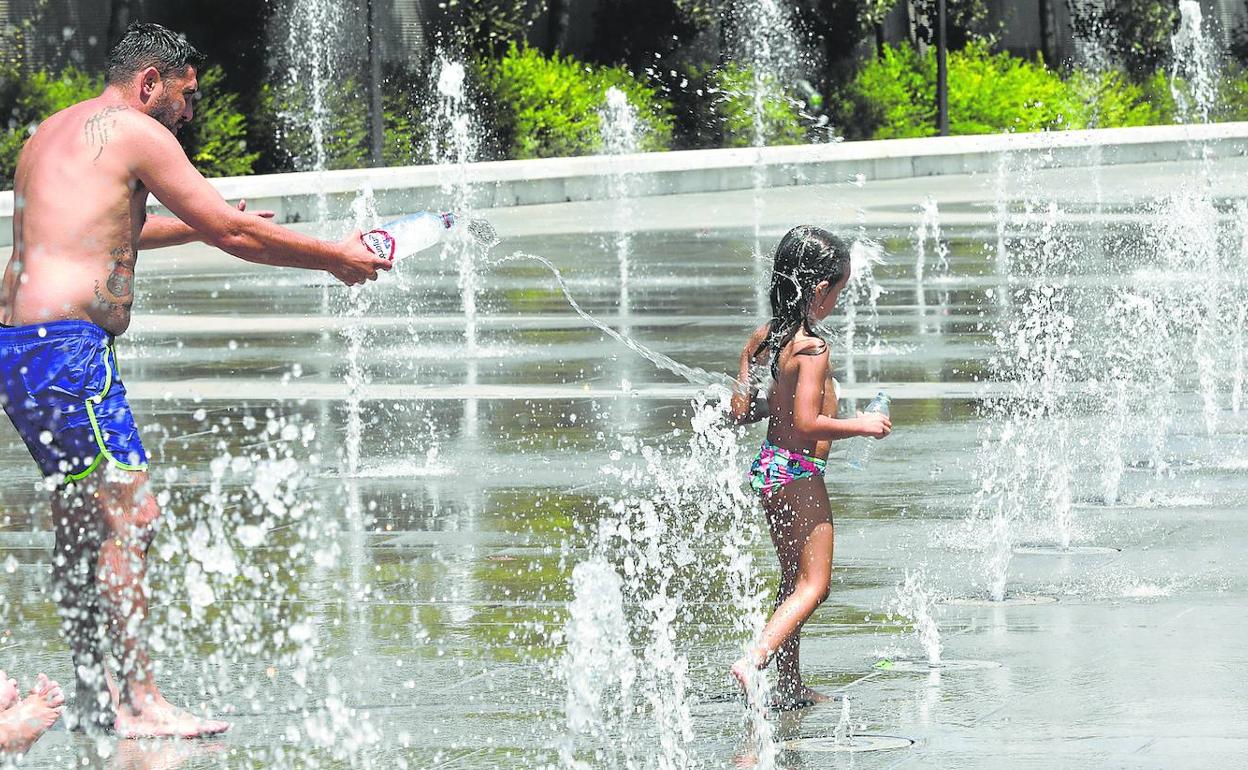 Un hombre y una niña se refrescan en una fuente.