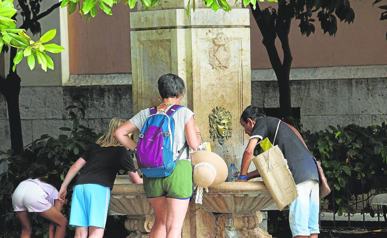 Varias personas se refrescan en una fuente situada junto a la plaza de la Virgen de Valencia. 