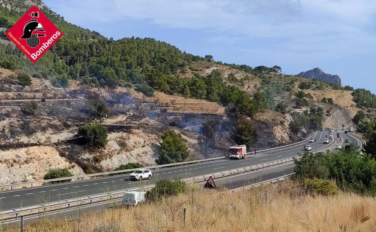 Los bomberos trabajando en la extinción del fuego junto a la autopista. 