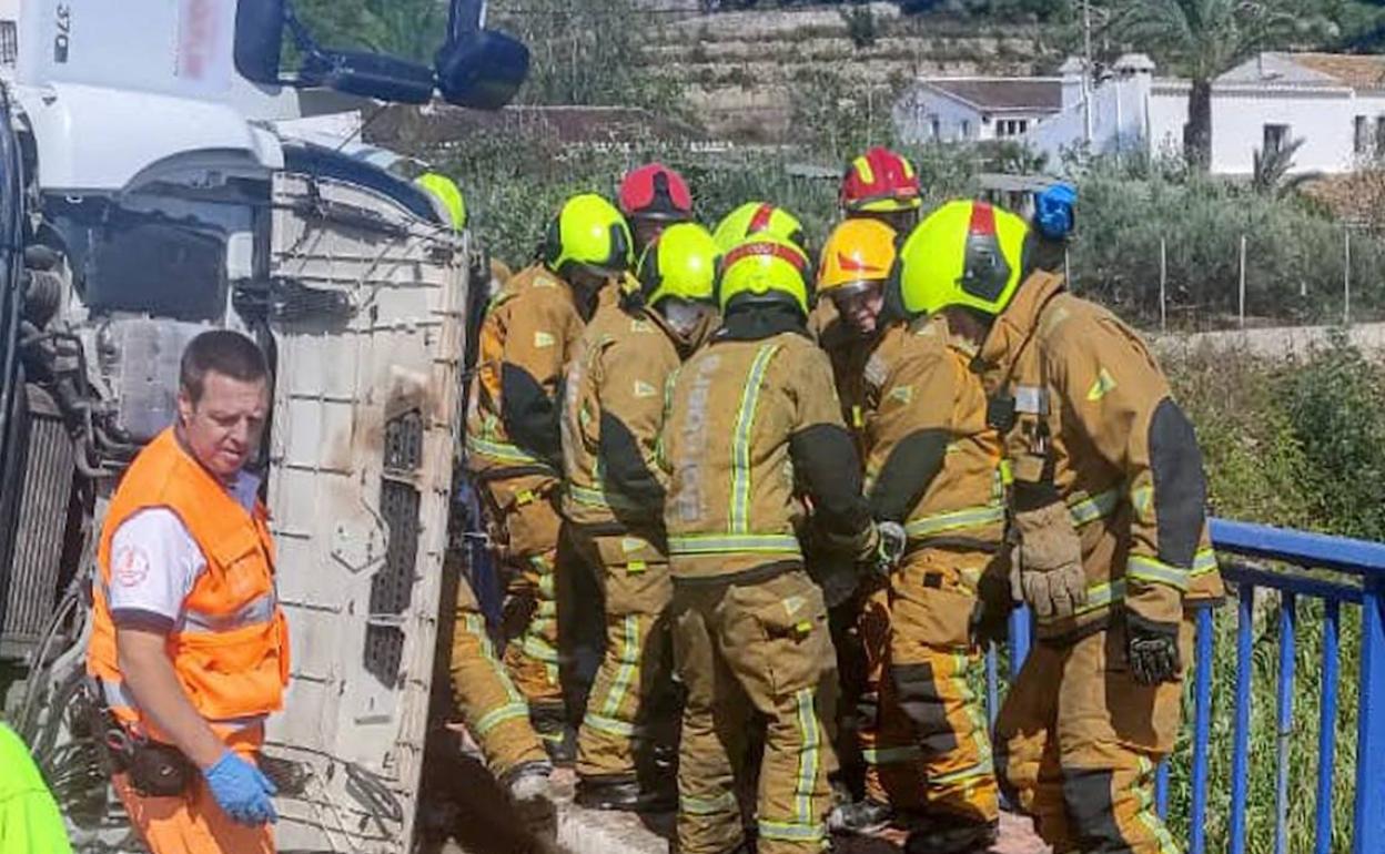 Los bomberos excarcelando al conductor tras volcar junto al puente. 