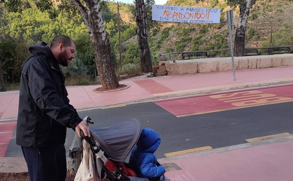 Un hombre con un carrito de bebé circula cerca de una pancarta reivindicativa. 