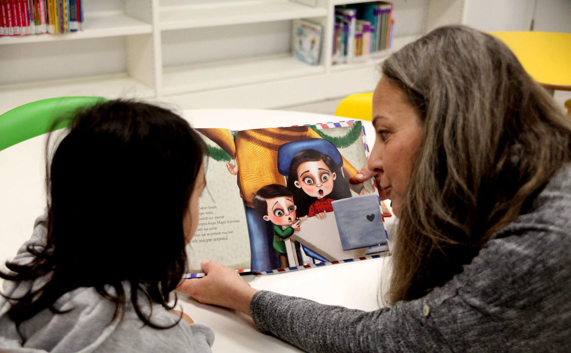 Candela, atenta al libro que le lee su madre Mónica en la biblioteca infantil de la Casa de Cultura de Dénia. 