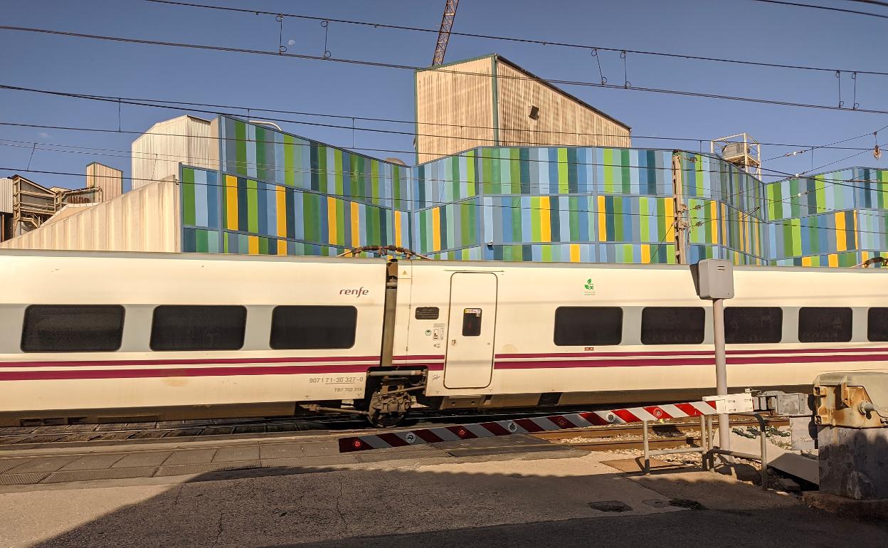 Un tren circula por Benifaió mientras el paso a nivel permanece cerrado. 