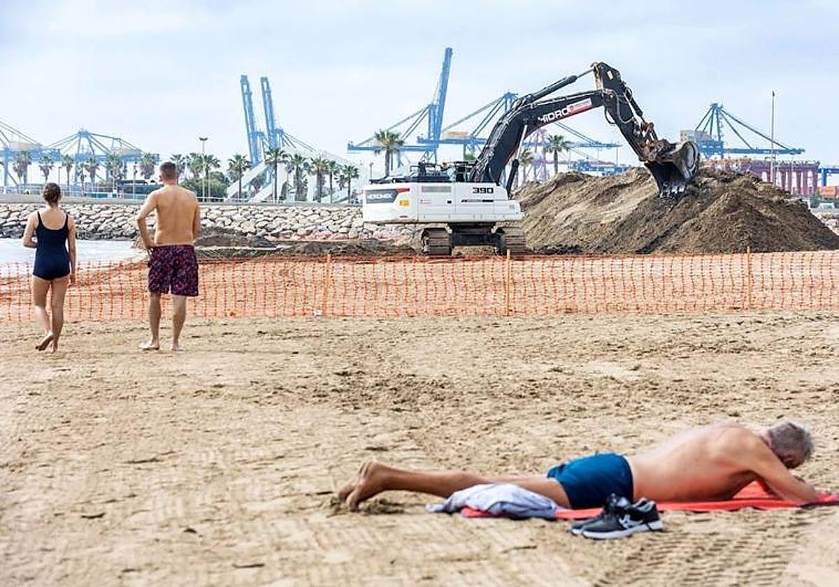 Un hombre toma el sol en el Cabañal ante montones de arena.
