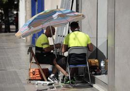 os operarios de telefonía se protegen con una sombrilla del intenso sol y calor, mientras tienen que trabajar en la calle., en Valencia.