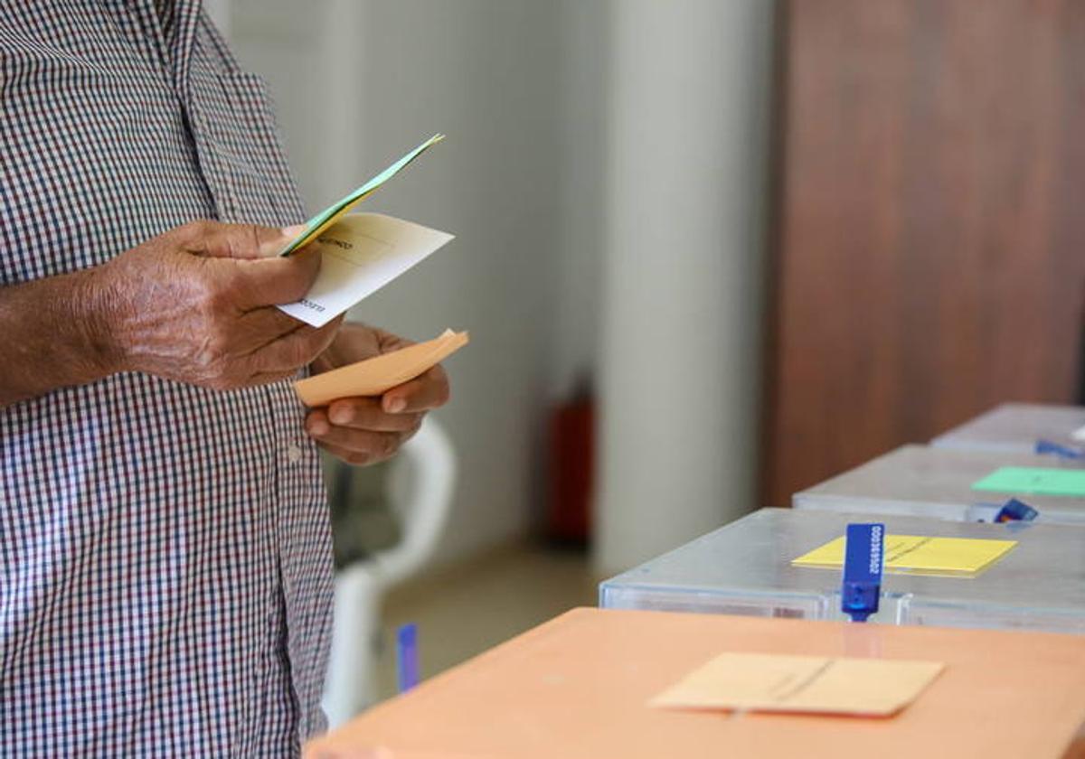 Un hombre sostiene sus papeletas de votación ante las urnas de la mesa en el colegio electoral.