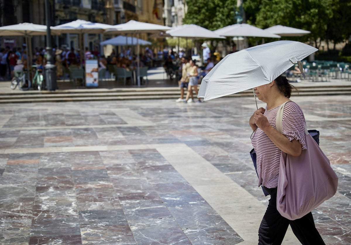 Una mujer se protege del sol y el calor en la plaza de la Virgen.