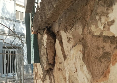 Imagen secundaria 1 - Carteles reivindicativos colocados por la AMPA y desperfectos en la parte exterior del muro perimetral. Se observan zonas donde la piedra se está desgajando, grietas y reparaciones anteriores. 