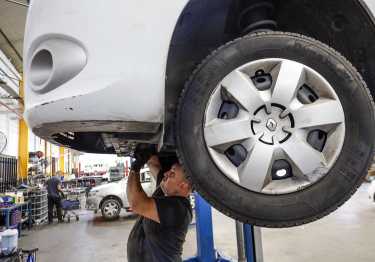 Un mecánico revisa los bajos de un coche en un taller de Valencia.