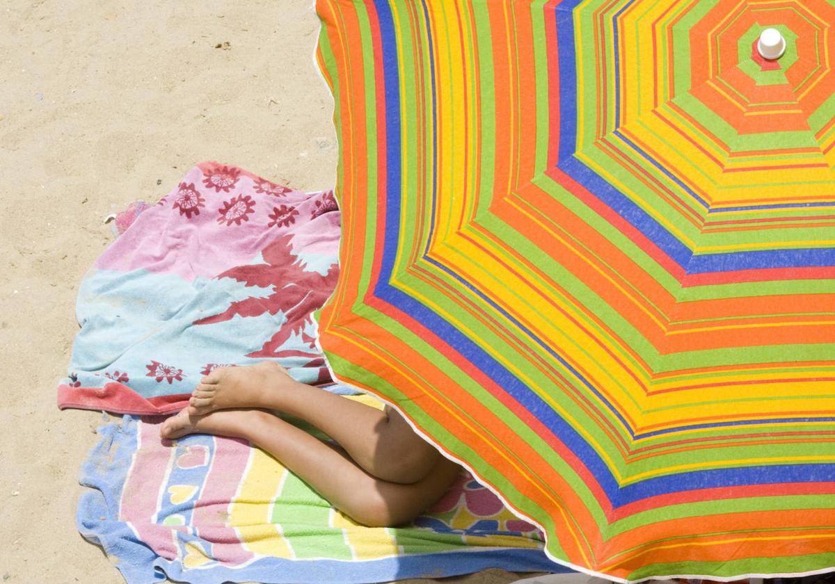 Unas piernas asoman por debajo de una sombrilla en una playa