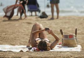 Una mujer consulta el teléfono móvil en la playa.