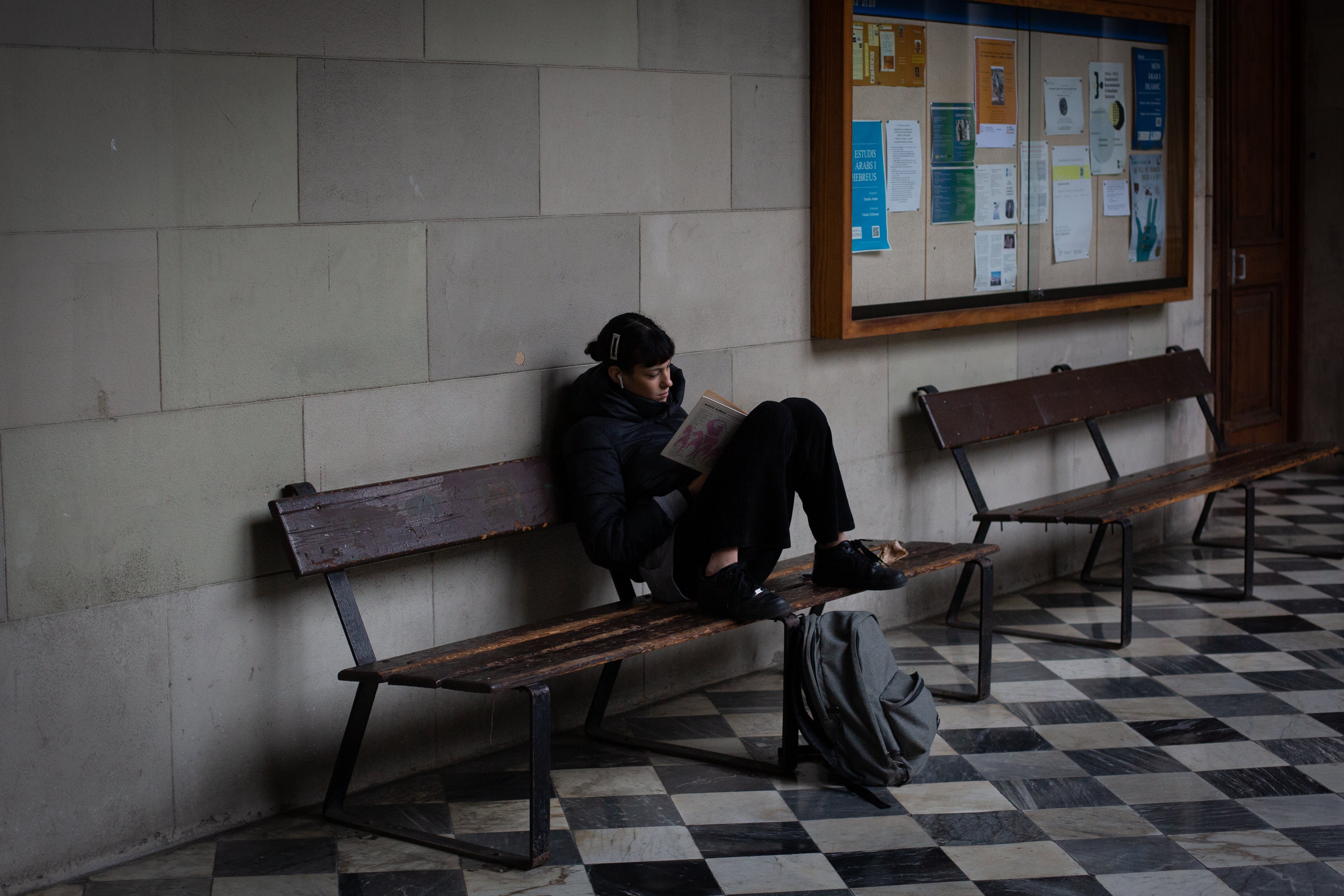 Un adolescente lee en un banco en el patio de un instituto.