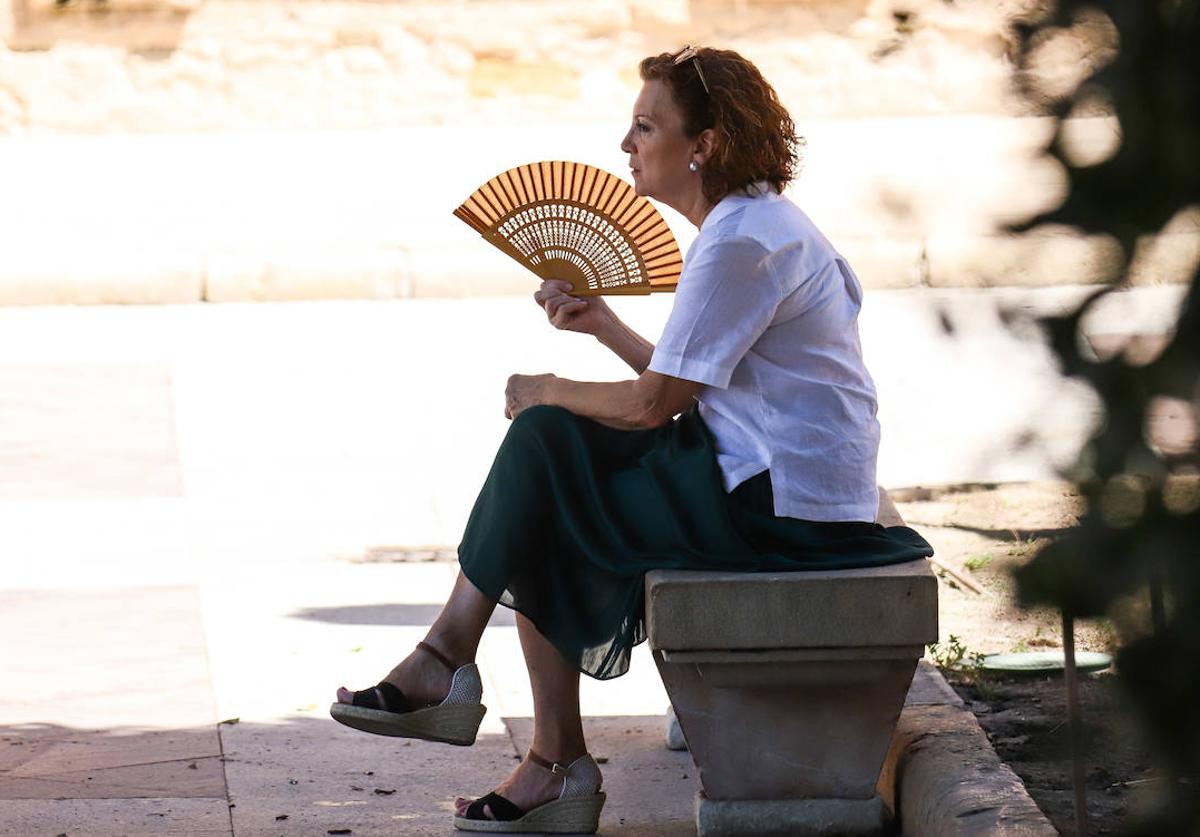 Una mujer alivia las altas temperaturas a la sombra, con un abanico.