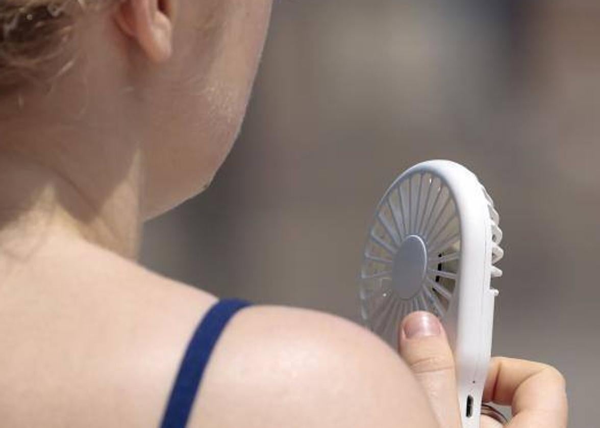 Una joven se refresca con un ventilador de mano,