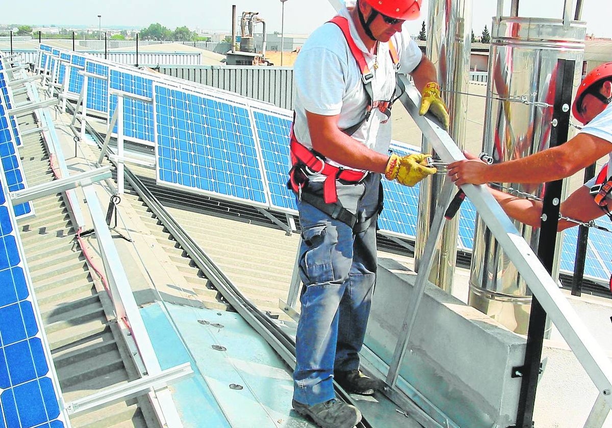 Dos operarios manipulan placas solares fotovoltaicas en la cubierta de un edificio.