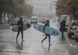 Dos surfistas caminan bajo la lluvia en una imagen de archivo.