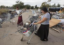 Denisa y Mura, madre e hija, entre montañas de chatarra, con los carros que usan para ganarse el pan y sus casas detrás, en una planta ilegal junto al polígono Vara de Quart.