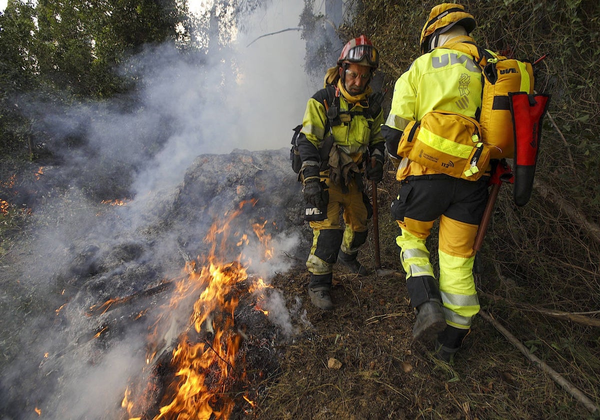 Dos bomberos intentan sofocar las llamas en el incendio de Montitxelvo.