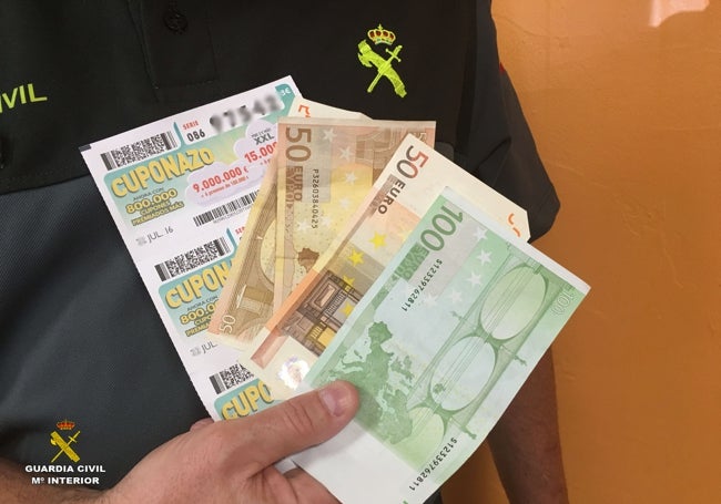 Un guardia civil muestra dinero y cupones falsos intervenido a un timador.