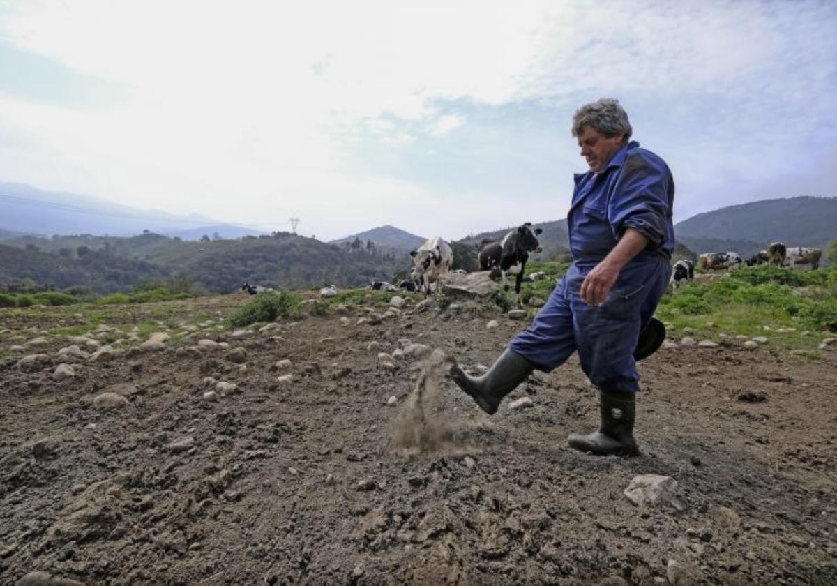 Un agricultor y ganadero levanta con el pie un poco de tierra para mostrar lo seca que está.