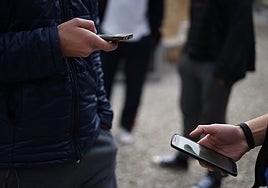 Dos jóvenes miran sus teléfonos móviles.