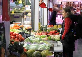 Una mujer, frente a un puesto de frutas y verduras en un mercado.