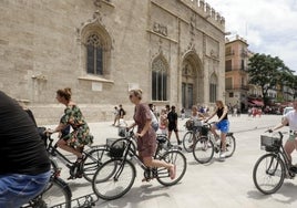 Un grupo de turistas en bicicleta por la plaza del Mercado frente a la Lonja.