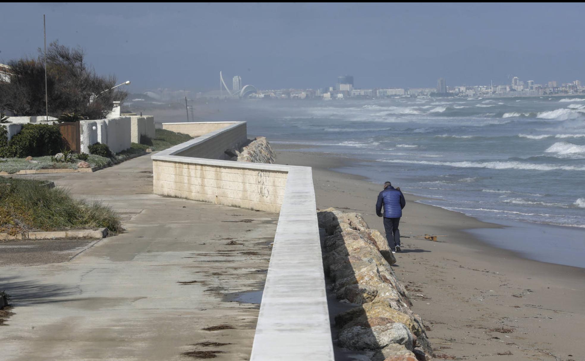 Un hombre pasea por la playa con la ciudad de Valencia al fondo. 