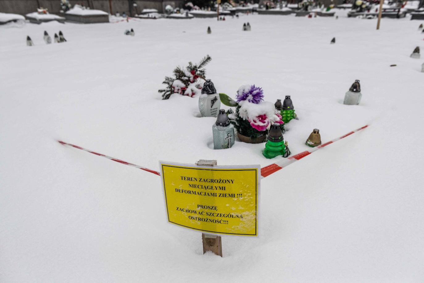 Un cartel de advertencia que dice: 'Área con peligro de deformaciones de la tierra no continuas. Por favor, tenga mucho cuidado'. Se encuentra en el lugar vacío del cementerio local donde el suelo se derrumbó.