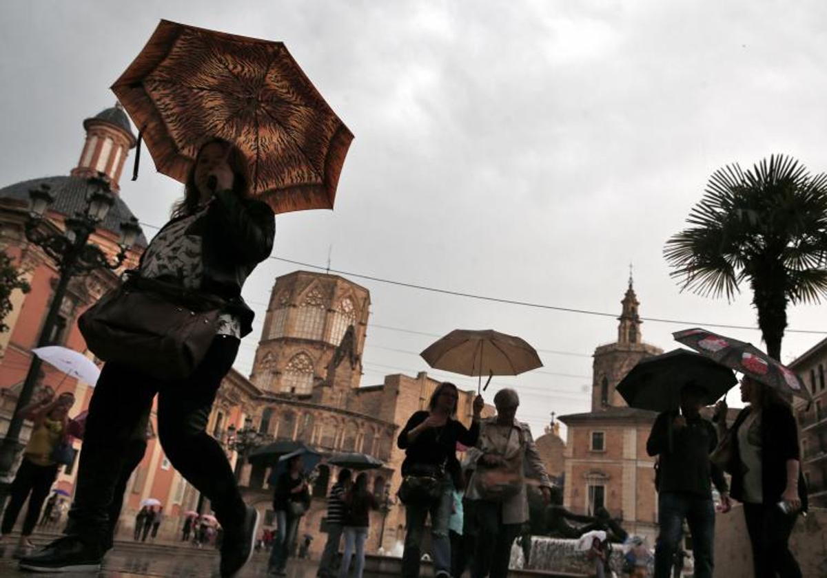 Unas personas atraviesan al plaza de la Virgen de Valencia bajo la lluvia, en una imagen de archivo.