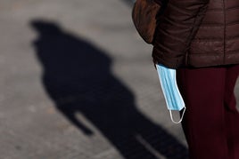 Una persona pasea con una mascarilla en la mano por la calle.