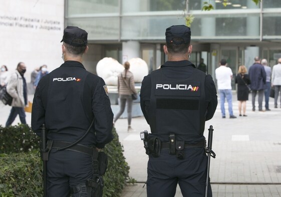 Dos agentes de la Policía Nacional vigilan la Ciudad de la Justicia, junto a una fila de ciudadanos.