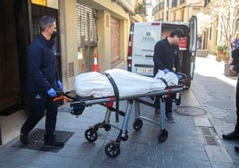 Dos empleados del retén fúnebre sacan el cadáver del edificio.