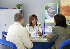 Una pareja es informada sobre un préstamo hipotecario en el departamento financiero de una sucursal.