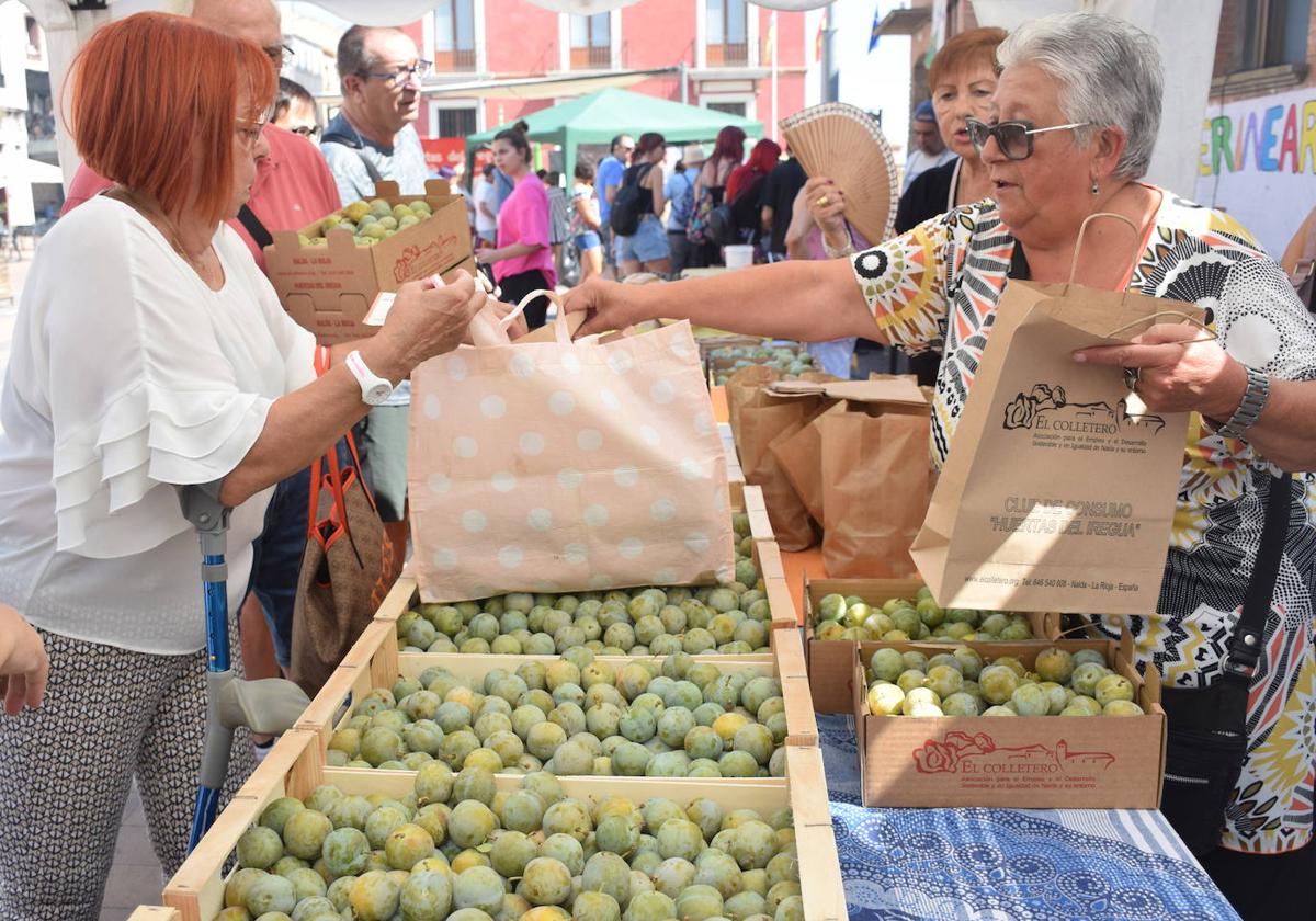 Varias personas comprando ciruelas en un supermercado.