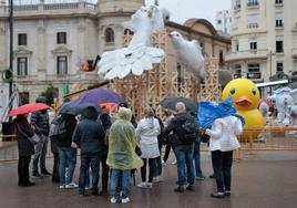 Grupos de personas se dan cita en la plaza del Ayuntamiento para ver la mascletà a pesar del mal tiempo.