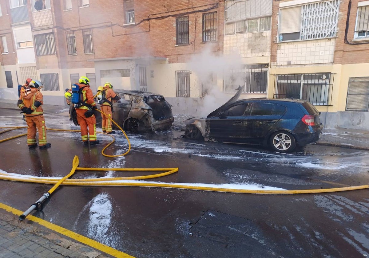 Los bomberos apagan los coches incendiados.